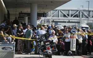 Delayed passengers stand behind a police cordon after a shooting incident at Los Angeles airport