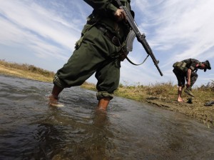 A soldier from the Kachin Independence Army puts on his shoes as he and his comrade cross a stream towards the front line in Laiza