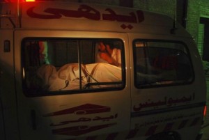 A man sits beside the body of a woman who was killed on board a PIA plane, as the ambulance carrying them arrives at a hospital in Peshawa
