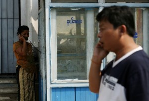 A man talks on his mobile phone next to a woman talking at a public phone shop in central Yangon